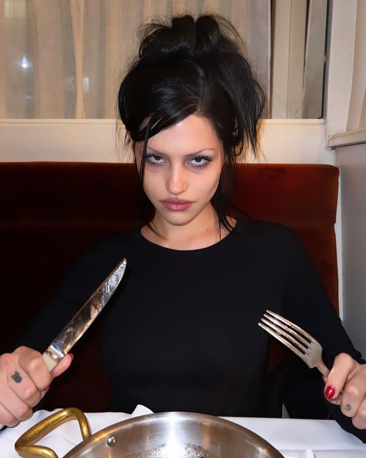 Gabbriette Bechtel holding a fork and knife sitting in front of a dining table with half of a bowl being seen.